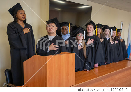 Graduates stand proudly at the ceremony with their hands over their hearts. Graduates stand proudly at the ceremony with their hands over their hearts. 132510341