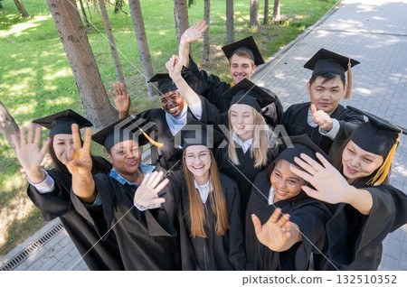 Students of different nationalities in graduation gowns wave their hands.  132510352