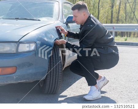 Caucasian man examines and tries to fix a deformation on the body of his car.  132510521