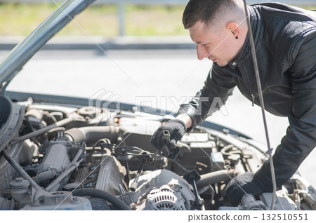 A man changes spark plugs in his car. A man changes spark plugs in his car. 132510551