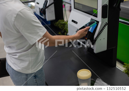 A woman pays using her smartphone at a self-checkout. A woman pays using her smartphone at a self-checkout. 132510552