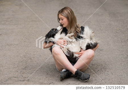 Young caucasian woman sitting on asphalt and hugging border collie dog.  132510579