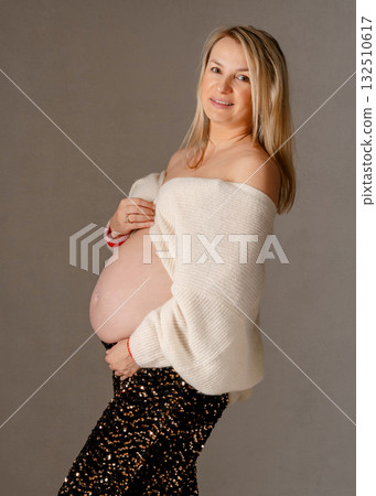 28 week, Warm studio portrait of a smiling expectant mother in cream knitwear, hands resting on her baby bump, joyful and intimate capture of pregnancy glow 132510617