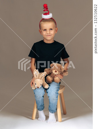 Cute boy wearing Christmas hat, holding teddy bears. Studio holiday portrait of childhood joy and warmth Cute boy wearing Christmas hat, holding teddy bears. Studio holiday portrait of childhood joy and warmth 132510622