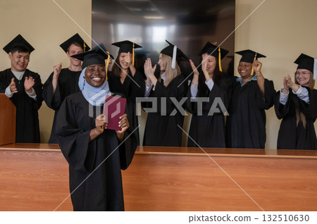Happy African woman in hijab receiving diploma and classmates applauding her. Happy African woman in hijab receiving diploma and classmates applauding her. 132510630