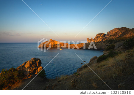 Quiet bay with sunlit rock and a solitary yacht 132510818