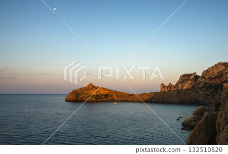 Yacht on calm sea near rocky coast at sunset 132510820