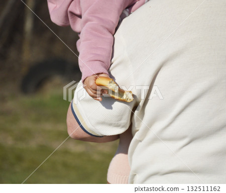 big bitten bagel in child's hand. adult man holds child in his arms 132511162
