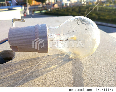 The light bulb hangs against a light concrete wall, illuminated by sunlight The light bulb hangs against a light concrete wall, illuminated by sunlight 132511165
