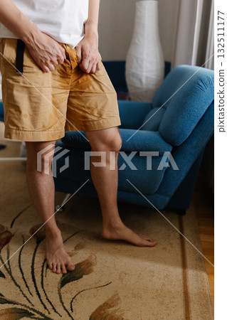Vertical cropped shot of unhealthy young man grappling with urinary incontinence, anxiously clutching wet pants as navigates discomfort and embarrassment of situation. Concept of healthy lifestyle. Vertical cropped shot of unhealthy young man grappling with urinary incontinence, anxiously clutching wet pants as navigates discomfort and embarrassment of situation. Concept of healthy lifestyle. 132511177