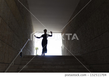 Woman dancing, emerging from dark passage into light 132511704