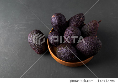 Dark, ripe avocados in wooden bowl on a rustic green surface. Dark, ripe avocados in wooden bowl on a rustic green surface. 132512760