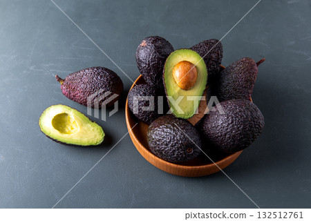 Dark, ripe avocados in wooden bowl on a rustic green surface. 132512761