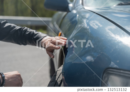 A Caucasian man inspects damage to his car.  132513132