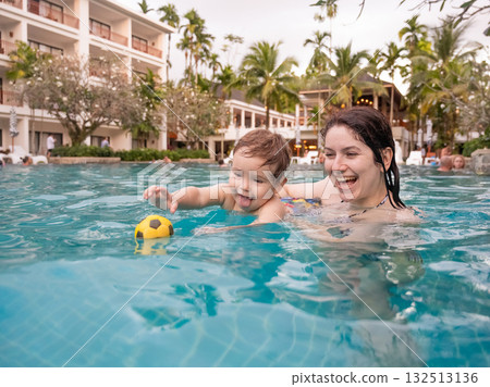 Caucasian woman holds her son while swimming in a pool on vacation. Mom teaches little boy to swim.  132513136