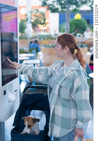 Caucasian woman makes a purchase at a self-service counter with a Jack Russell terrier dog in a stroller in a shopping center. 132513224