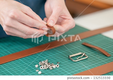 A woman attaches accessories to a leather belt. Leatherworker's workshop.  132513330