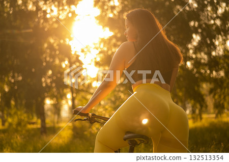 A Caucasian woman in yellow leggings and a crop top rides a bicycle in tights in the park. A Caucasian woman in yellow leggings and a crop top rides a bicycle in tights in the park. 132513354