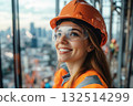 Female construction worker, young caucasian woman smiling on urban site with orange safety gear and helmet 132514299