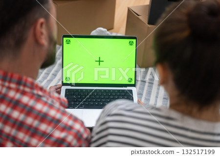 Digital Relocation: Hands with a laptop featuring an empty green mock-up screen, set against cardboard boxes in a living room, as a young couple moves to a new home Digital Relocation: Hands with a laptop featuring an empty green mock-up screen, set against cardboard boxes in a living room, as a young couple moves to a new home 132517199