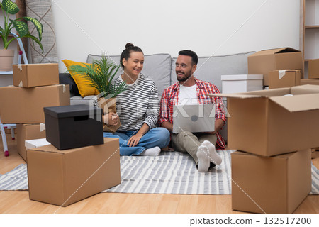 New Chapter: Young couple in their fresh home, amid boxes, uses a laptop to decide on interior design, shop online, or arrange moving services New Chapter: Young couple in their fresh home, amid boxes, uses a laptop to decide on interior design, shop online, or arrange moving services 132517200