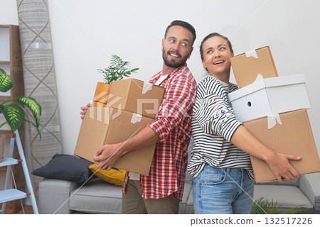 Settling as Tenants: A young couple moves to their new apartment, holding a pile of cardboard boxes in the living room, marking the start of their tenancy 132517226