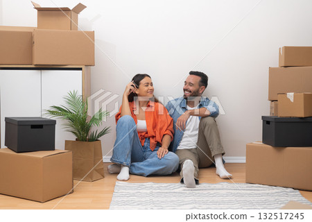 Joyful young couple in their freshly rented apartment, happily looking to each other with moving boxes. Bright, modern living space filled with promise Joyful young couple in their freshly rented apartment, happily looking to each other with moving boxes. Bright, modern living space filled with promise 132517245