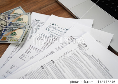 Tax forms and dollar bills on a wooden desk with a laptop. Financial management, tax refund, and accounting concept. Tax forms and dollar bills on a wooden desk with a laptop. Financial management, tax refund, and accounting concept. 132517256