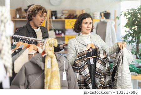 Woman choose jacket in store, exasperated husband accompanies his wife during shopping 132517696
