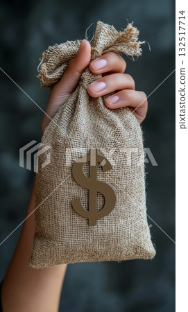 Hand is grasping a small burlap sack with a dollar sign on it, representing savings, investment, and financial growth 132517714