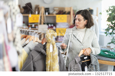European female customer examine and choose new coat or jacket for cold season in modern store 132517715