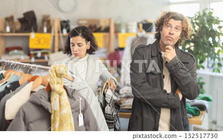 European female customer choose new jacket or coat for winter season, man bored or imitated while waiting for woman in clothing store 132517730