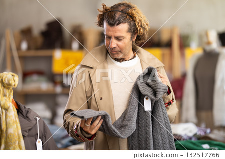 Handsome positive man client selecting new sweaters for cold season in clothing shop 132517766