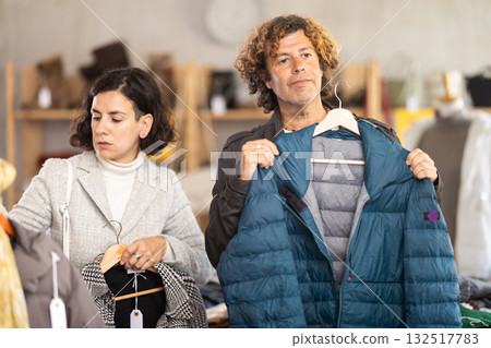 Happy european couple examine and choose new coat or down jacket for cold season in modern store Happy european couple examine and choose new coat or down jacket for cold season in modern store 132517783