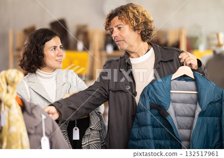Man choose down jacket in store, wife give advice and help to choose goods. Man choose down jacket in store, wife give advice and help to choose goods. 132517961