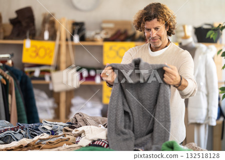 Handsome positive man client selecting new sweaters for cold season in clothing shop 132518128