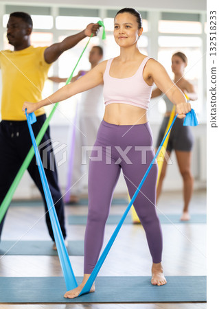 Asian girl conducts Pilates for multinational students, standing exercises with wide elastic band Asian girl conducts Pilates for multinational students, standing exercises with wide elastic band 132518233