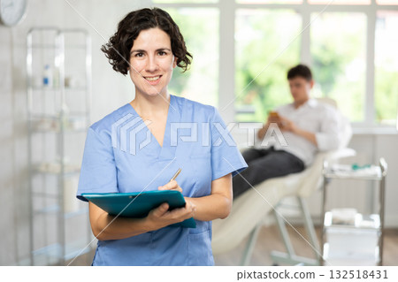 Middle-aged woman doctor posing in doctor's cabinet with document in hands 132518431