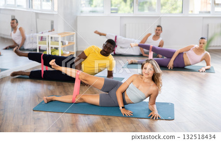 Group of multinational people training leg muscles using resistance bands during Pilates studio 132518434
