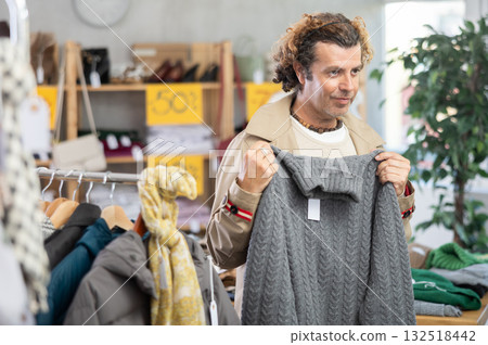 man stands near the counter with clothes and chooses a sweater man stands near the counter with clothes and chooses a sweater 132518442