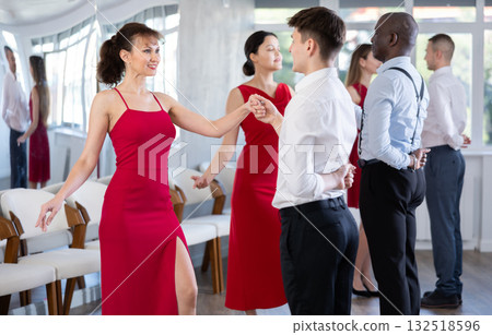 Beautiful girls dressed in red dress dancing waltz with partners in dancing class during multinational group party 132518596