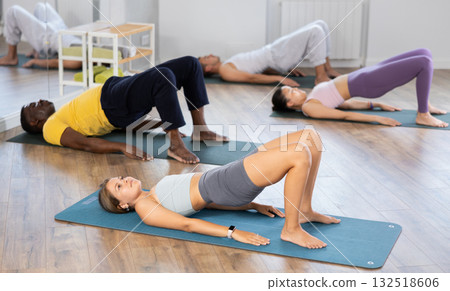 Girl performing glute bridge on mat during group pilates class Girl performing glute bridge on mat during group pilates class 132518606