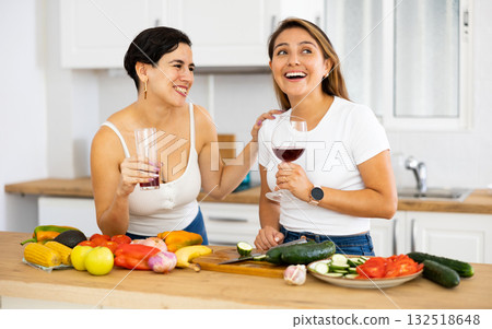 Two cheerful female roommates drinking wine and preparing dinner at home Two cheerful female roommates drinking wine and preparing dinner at home 132518648