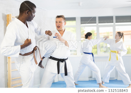 Middle-aged man attendee of karate classes fighting with his opponent in sports hall Middle-aged man attendee of karate classes fighting with his opponent in sports hall 132518843