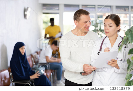 Doctor in a white coat discusses documents with a man in the lobby of clinic 132518879