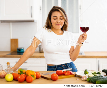 Portrait of woman with glass of red wine in modern kitchen - housewife prepares a vegetable salad and drinks red wine Portrait of woman with glass of red wine in modern kitchen - housewife prepares a vegetable salad and drinks red wine 132518929