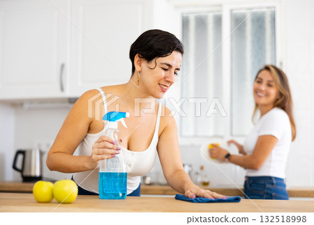 Woman cleaning countertop in kitchen while friend washes dishes Woman cleaning countertop in kitchen while friend washes dishes 132518998