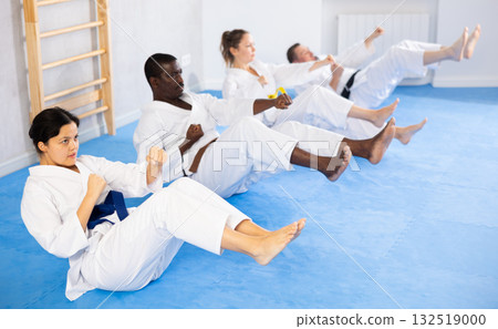 Multinational women and men in kimono train abdominal muscles and do punches at the same time during karate training Multinational women and men in kimono train abdominal muscles and do punches at the same time during karate training 132519000