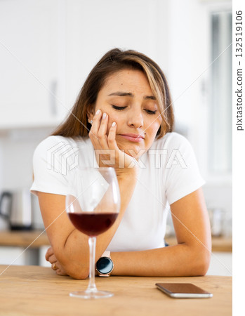 Frustrated young woman drinking wine and waiting for call in home kitchen 132519106