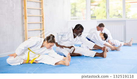 Teacher and cosmopolite followers perform warm-up exercises and legs stretching 132519118